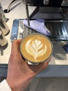Verse cappuccino met latte art in de hand bij de machine
