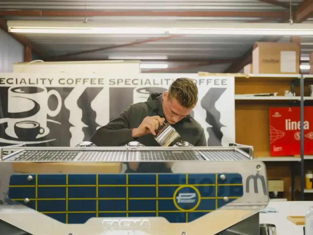 Jordy giet melk achter de espressomachine bij het NK Latte Art