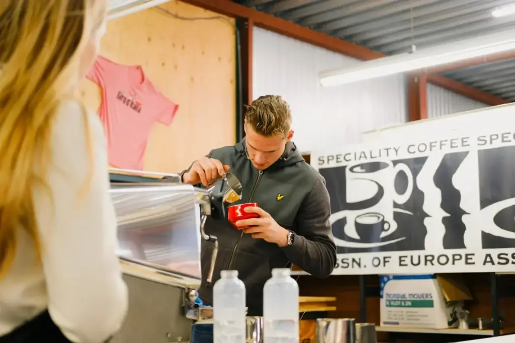 Barista Jordy giet latte art in een rode kop achter de espressomachine