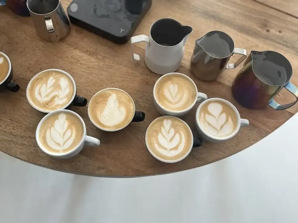 Kopjes met latte art en melkkannen op een tafel