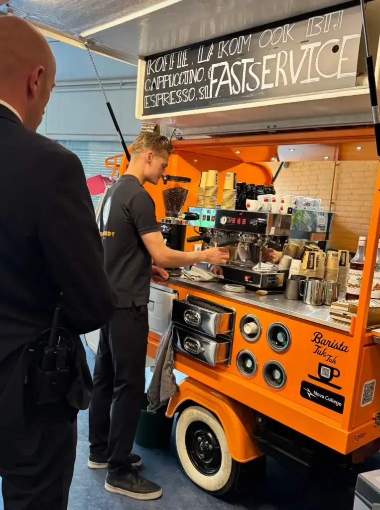 Jordy zet koffie achter de koffie-Piaggio van het Nova College